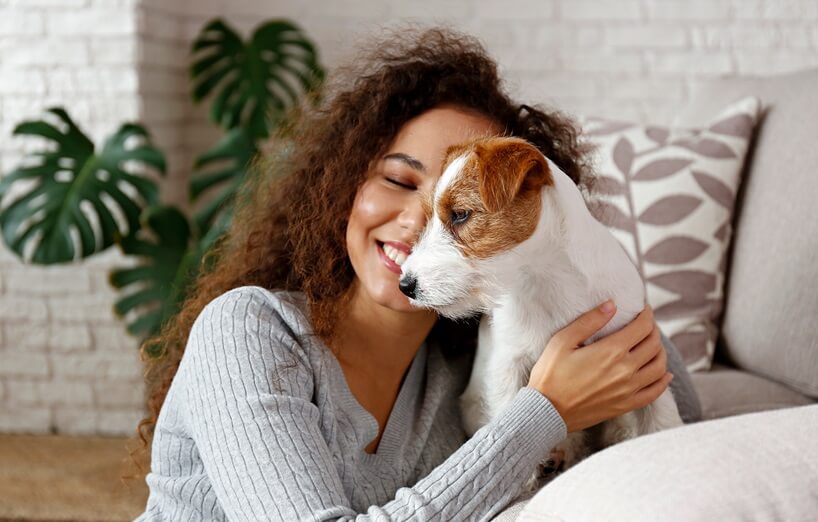 Frau kuschelt liebevoll mit einem kleinen weißen Terrier auf dem Sofa