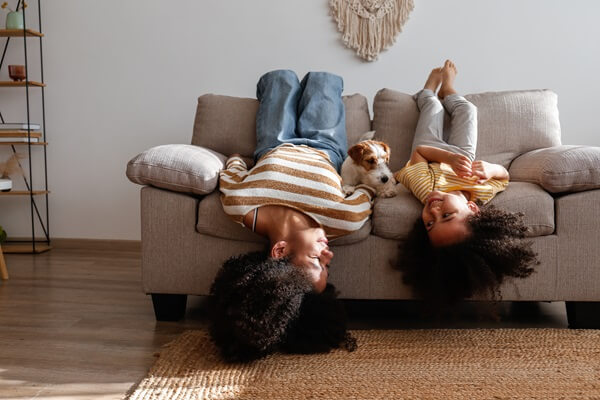 Zwei Frauen liegen kopfüber auf dem Sofa und schauen den Parson Russel Terrier an, der zwischen ihnen liegt.